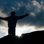 Silhouette view of a person with open arms at sunrise, symbolizing freedom and peace.